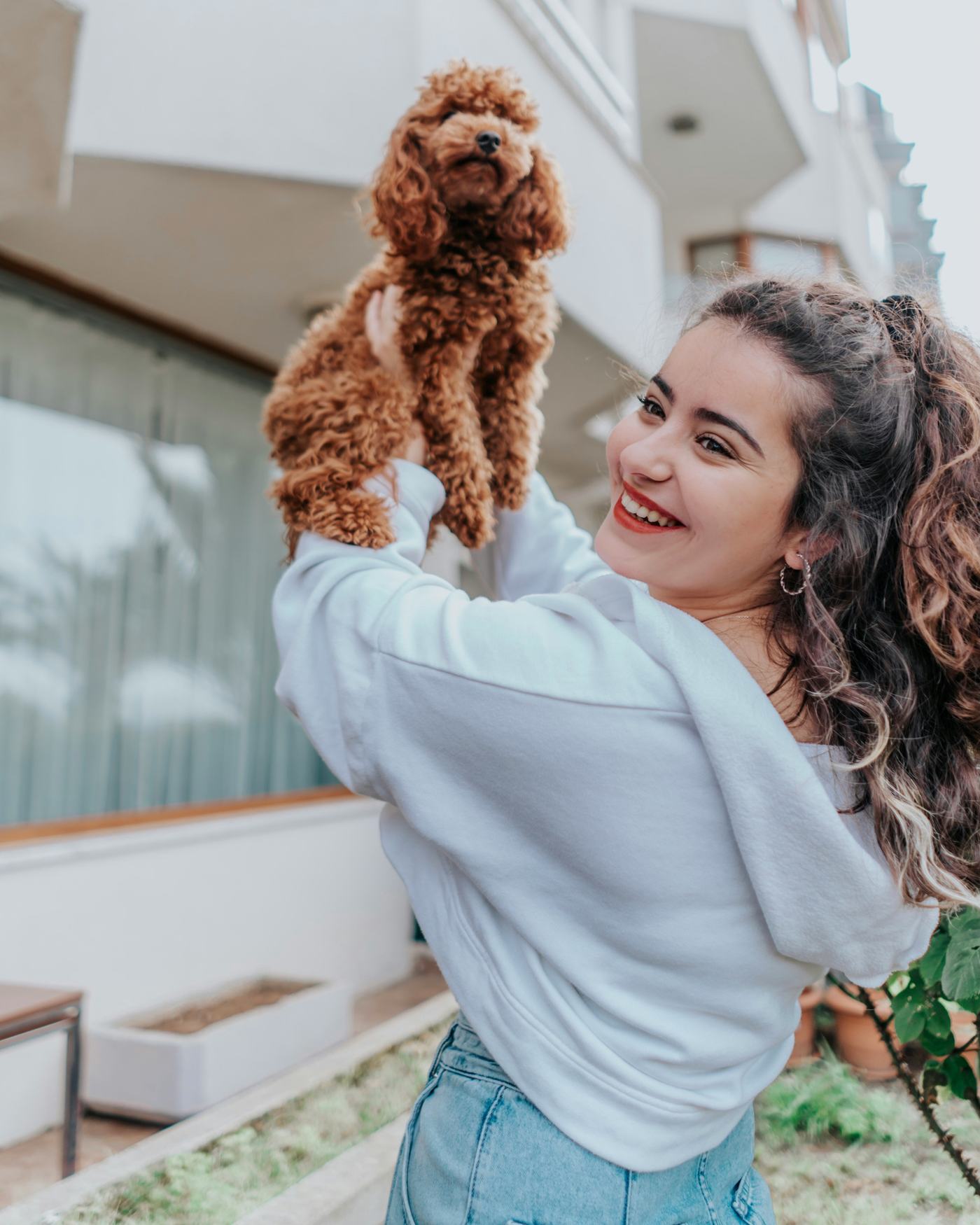 Smiling woman lifting up her toy poodle outdoors
