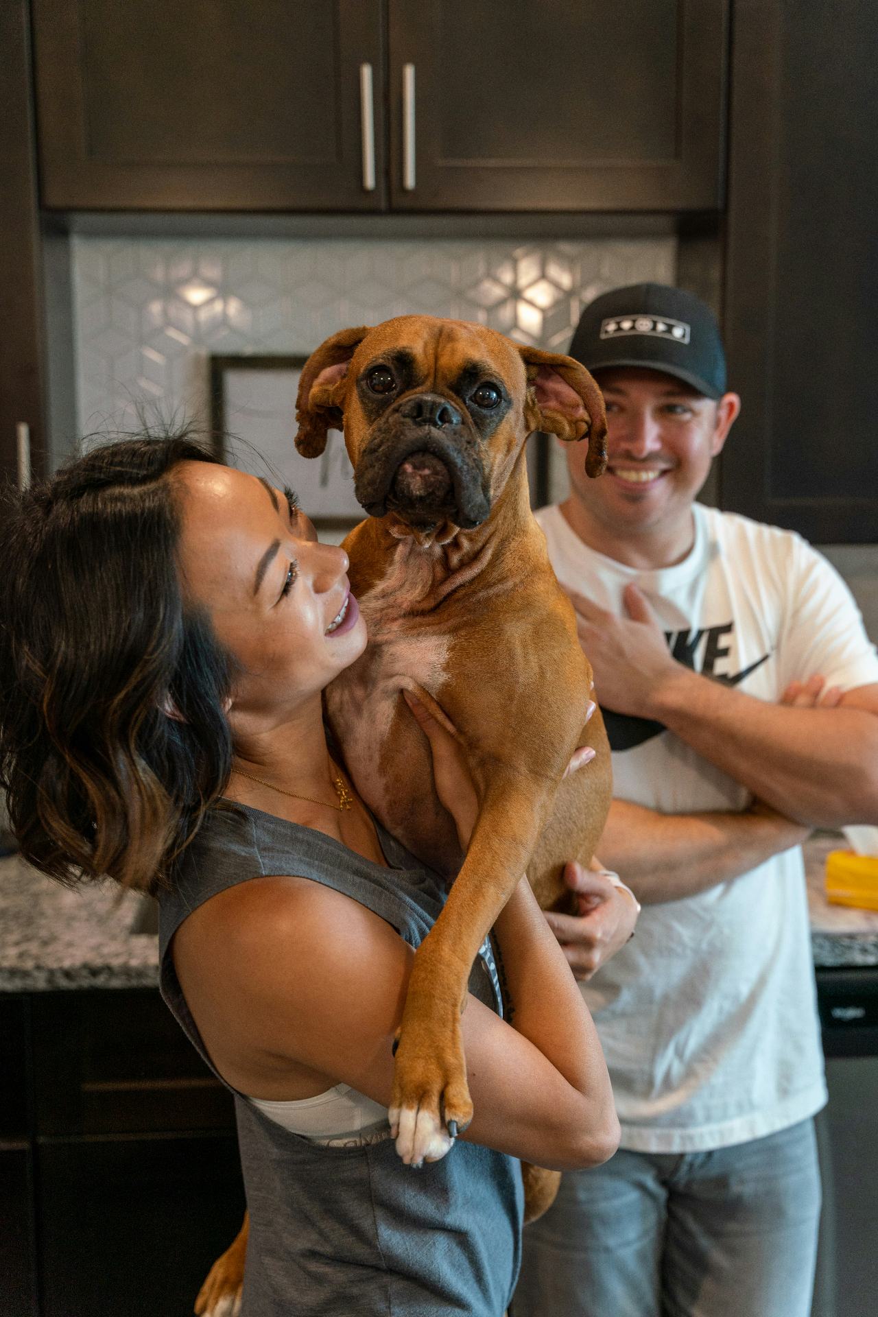 Couple in their kitchen lifting up their boxer dog